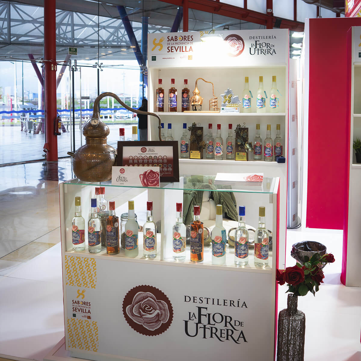Expositor de anises artesanales de la destilería Flor de Utrera en el Salón H&T Málaga 2025, con alambique tradicional y botellas de licor en primer plano.